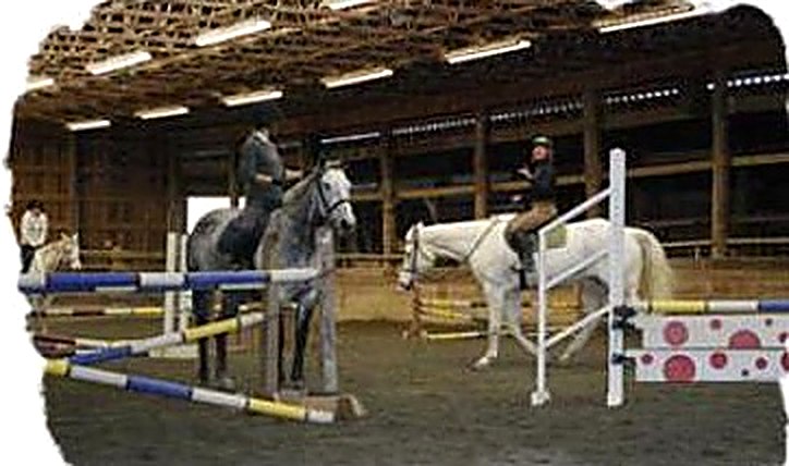 Riders training over jumps in the indoor arena